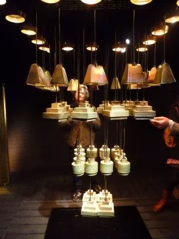 Instalación de lámparas colgantes de pantallas escalonadas sobre fondo oscuro en la Feria del Mueble de Milán