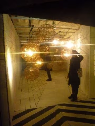 Esferas de luz dorada colgadas en una sala con suelo de franjas en zigzag en la Feria del Mueble de Milán