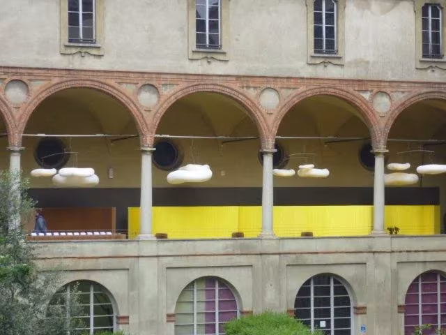 Claustro de arcos de ladrillo con nubes de lámparas de Molo sobre un tabique amarillo en Milán