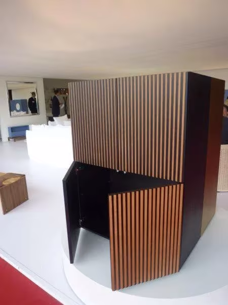 Pieza de mobiliario de listones de madera y paneles negros en un stand del Salone del Mobile de Milán