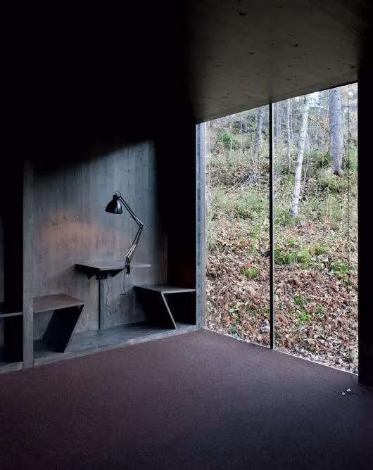 Juvet-Landscape-Hotel-in-the-Norwegian-wilderness-21 Interior de madera oscura del Juvet Landscape Hotel con un escritorio junto a una vidriera al bosque