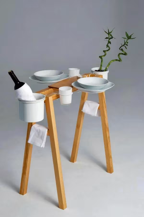 Mesa auxiliar de madera de patas finas con vajilla blanca, botella de vino y una planta de bambú