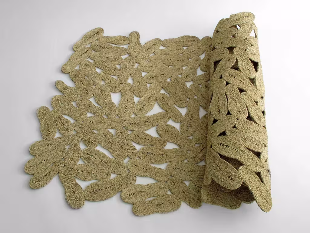 Alfombra Trepitjada de Martín Azúa de fibra natural calada con motivos de huellas, parcialmente enrollada