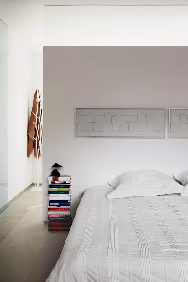 Belen Imaz +naturales 026 Dormitorio principal de la Casa Cambrils con cama blanca, libros apilados como mesilla y lámina enmarcada