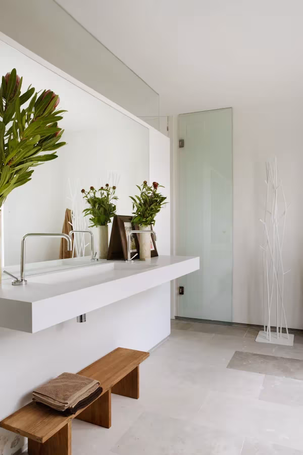 Belen Imaz +naturales 031 Baño de la Casa Cambrils con lavabo blanco corrido, plantas, mampara de vidrio y banco de madera
