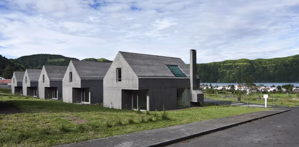 Viviendas de Souto de Moura en Sete Cidades, Azores: casas grises a dos aguas en hilera junto a una calle