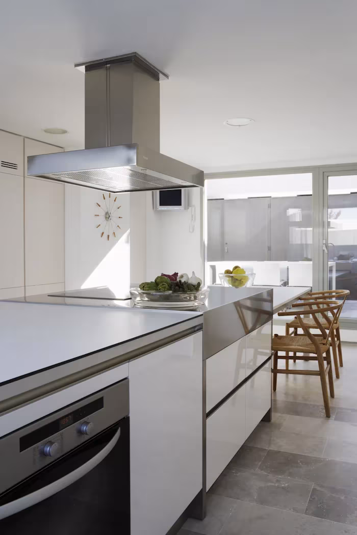 _X5C4706_1 Cocina blanca con isla de acero, campana central y taburetes de madera en el Ático en U de Ábaton