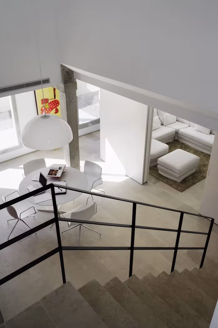 _X5C4840 Escalera con barandilla negra que desciende a una zona de estar con mesa redonda y lámpara blanca en el Ático en U de Ábaton