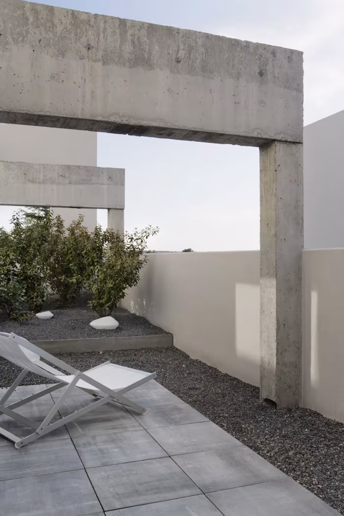 _X5C4895 Pórtico de hormigón visto sobre una terraza con gravilla, losas grises y tumbona blanca en el Ático en U