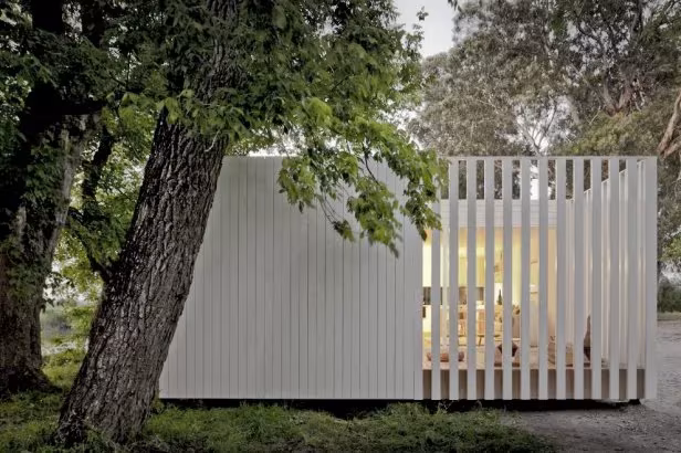 4a38ff89 Volumen blanco de lamas de madera junto a un gran tronco, con el interior iluminado, en Treehouse Riga