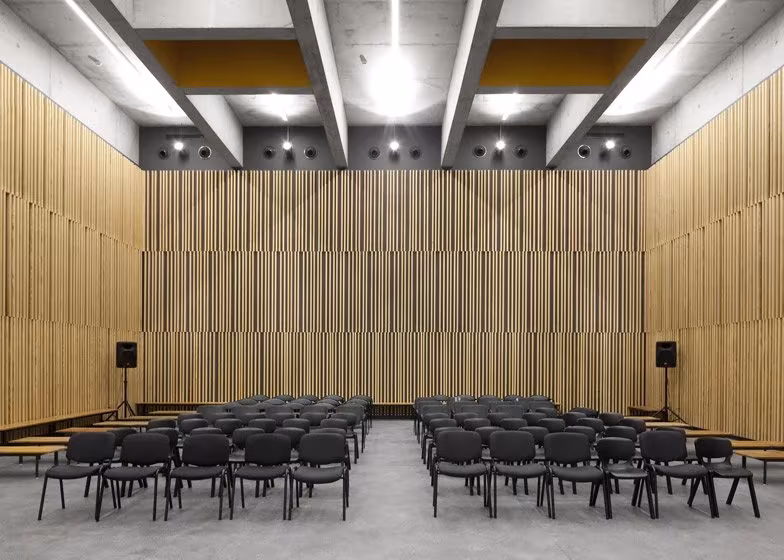 02ed06f6 Salón de actos de la escuela Braamcamp Freire con paneles de listones de madera y techo de vigas de hormigón