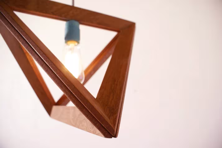 Detalle de una lámpara Lighframe en caoba con la bombilla encendida sobre fondo claro