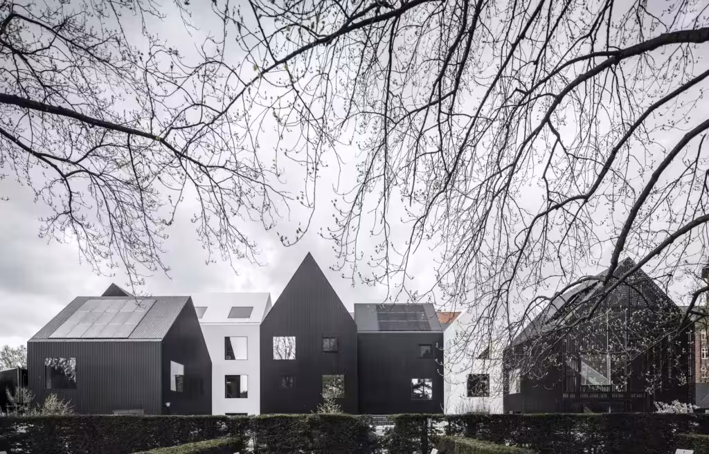 Guardería Frederiksvej de COBE en Copenhague: casitas negras a dos aguas bajo ramas desnudas