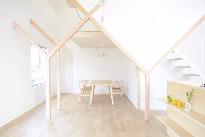 Comedor de la Casa H con mesa de madera bajo vigas en Y y una escalera blanca al fondo