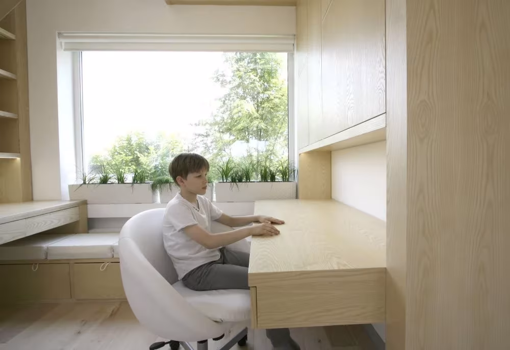 Niño en un escritorio de madera clara con silla blanca frente al ventanal en la residencia de Moscú