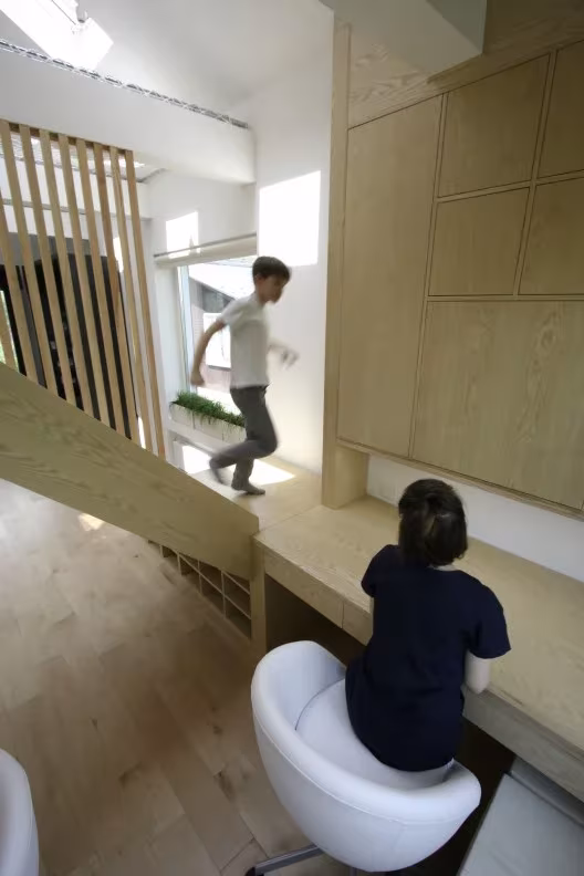 Niño bajando la escalera de listones mientras otro estudia en un escritorio con silla blanca