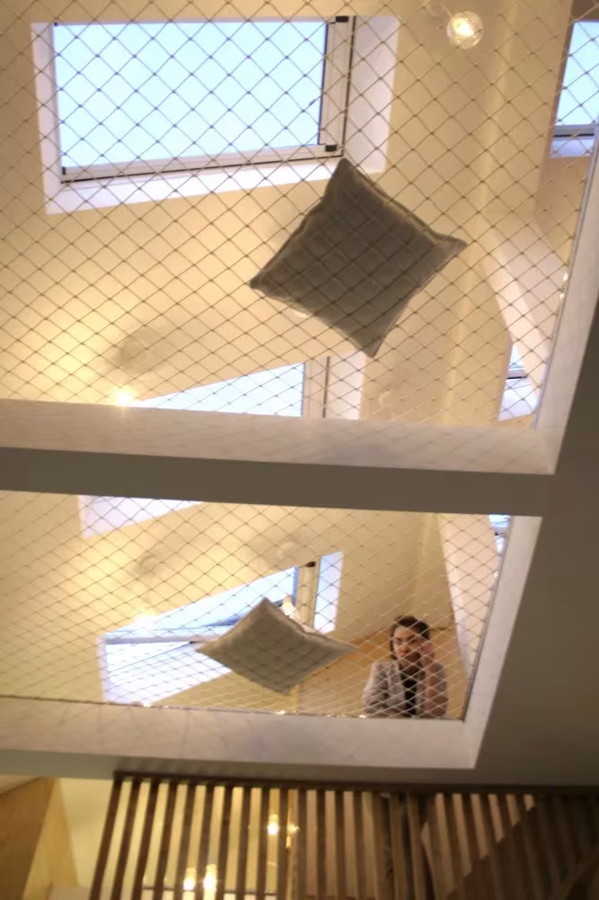 Cojines sobre la red del techo vistos desde abajo, con un niño asomado bajo los lucernarios