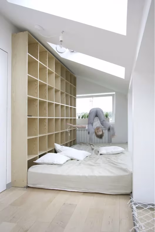 Cama baja junto a una estantería de madera de suelo a techo, con un niño colgado boca abajo