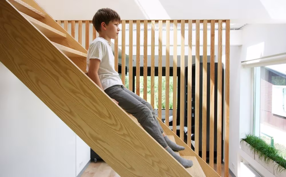 Niño deslizándose por la escalera de madera clara con barandilla de listones verticales
