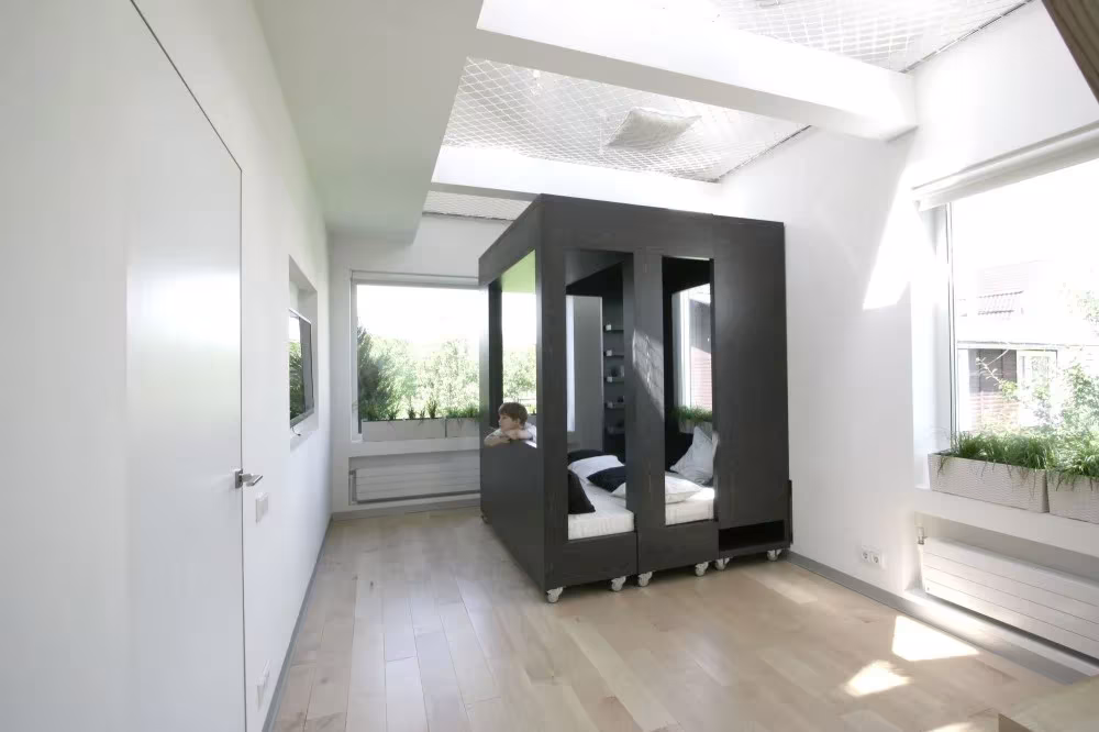 Cubo negro transformable sobre ruedas, abierto con cama en su interior, en el cuarto blanco de Moscú