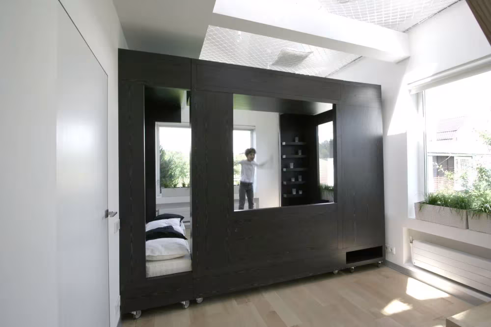 Cubo negro desplegado en dos módulos con estanterías y cama, junto al ventanal del cuarto de Moscú