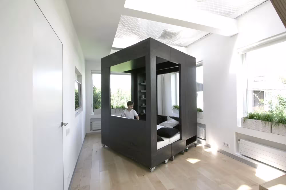Cubo negro transformable cerrado con un niño leyendo dentro, en el cuarto blanco con plantas