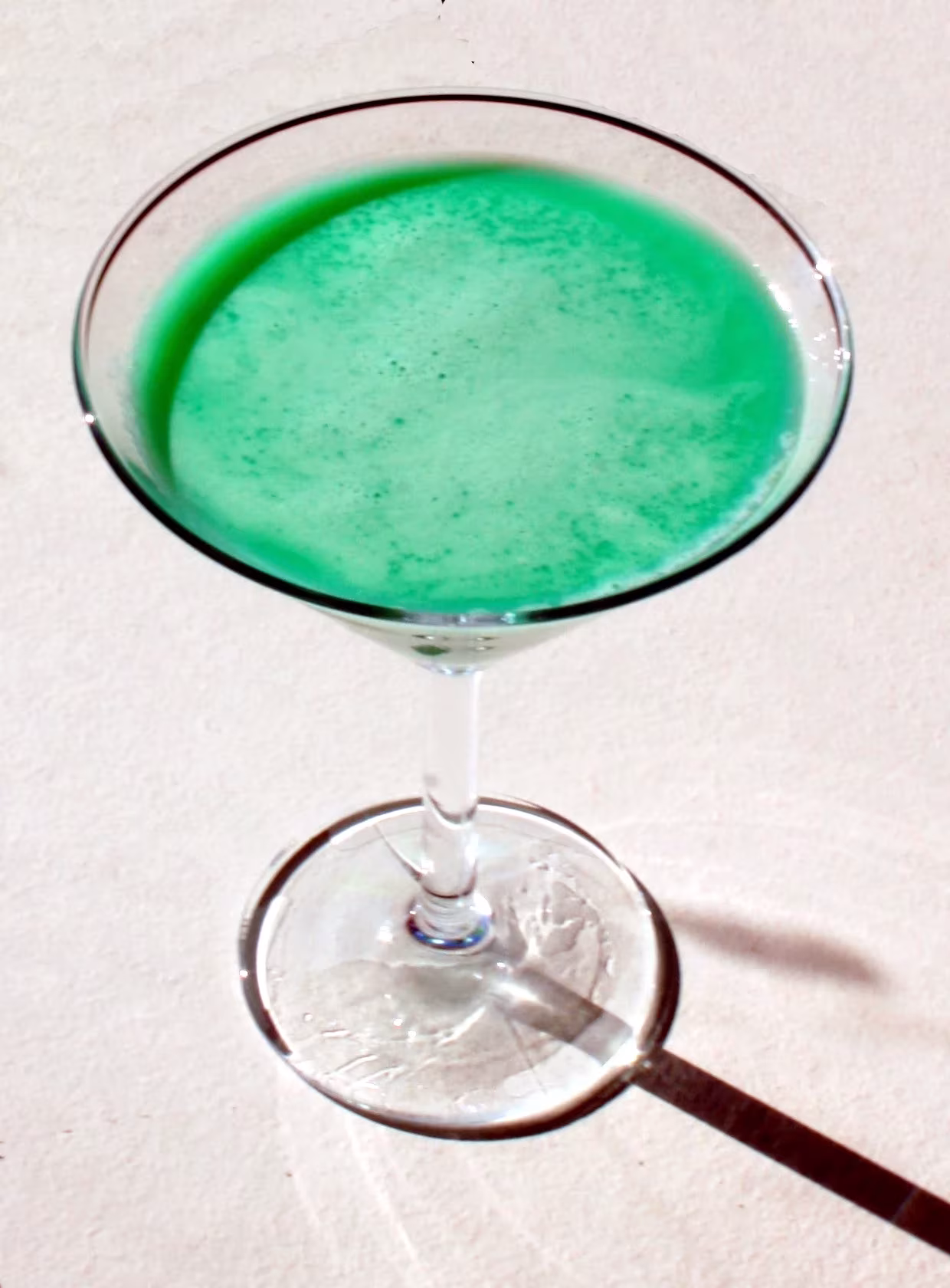 Cóctel de color verde menta servido en una copa de martini sobre fondo claro