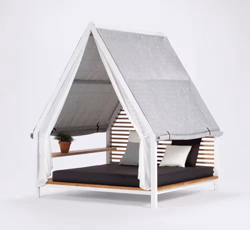 Cama de exterior Cottage de Kettal con la cubierta de tela gris cerrada, cojines blancos y una maceta