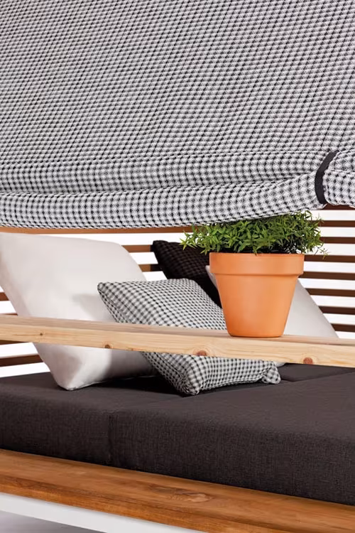 Detalle de la cama Cottage de Kettal: toldo de pata de gallo, cojines, estante de madera y maceta con planta