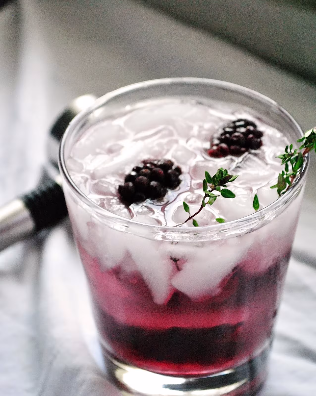 Cóctel Blackberry Gin Fizz en vaso bajo con hielo, moras y una ramita de tomillo