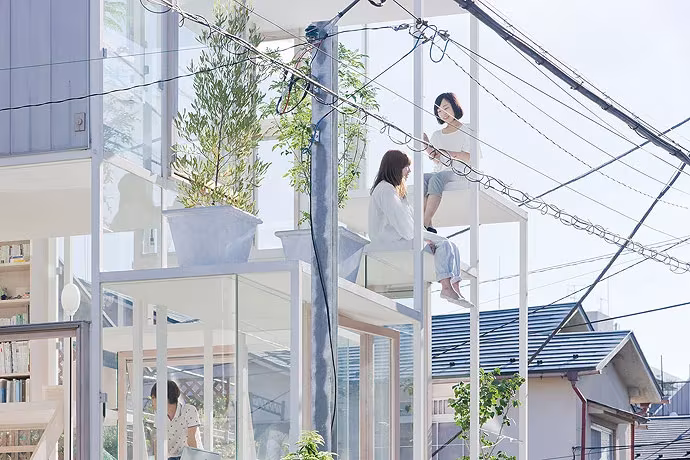 Casa Na de Sou Fujimoto en Tokio: estructura blanca y acristalada con dos personas sentadas en plataformas y plantas
