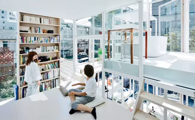 Interior de la Casa Na de Sou Fujimoto con estanterías de libros, plataformas blancas y paredes de vidrio