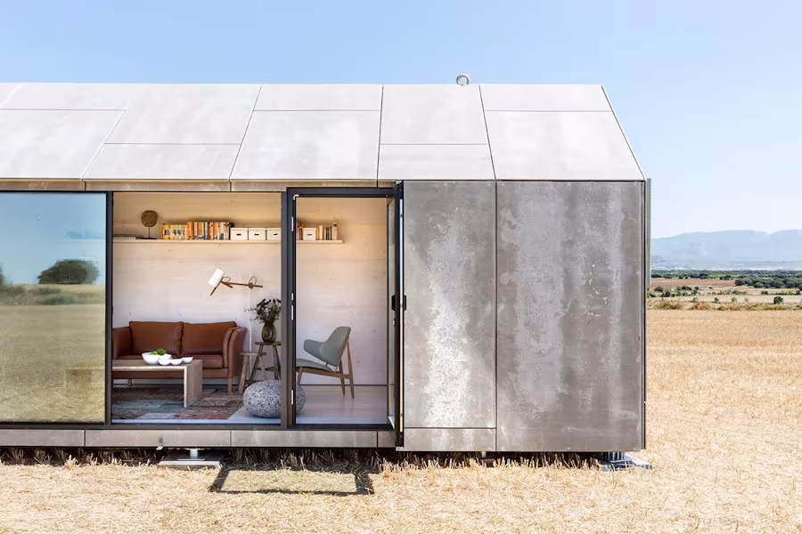Casa ÁPH80 de ÁBATON con grandes puertas de vidrio que dejan ver el salón amueblado en mitad del campo