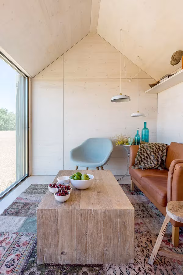 Salón de la casa ÁPH80 con paredes de madera clara, sofá de cuero, butaca azul y mesa baja maciza