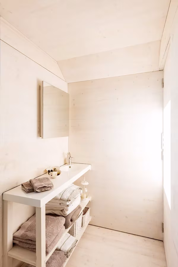 Baño de la casa ÁPH80 revestido de madera clara, con espejo y mueble blanco con toallas