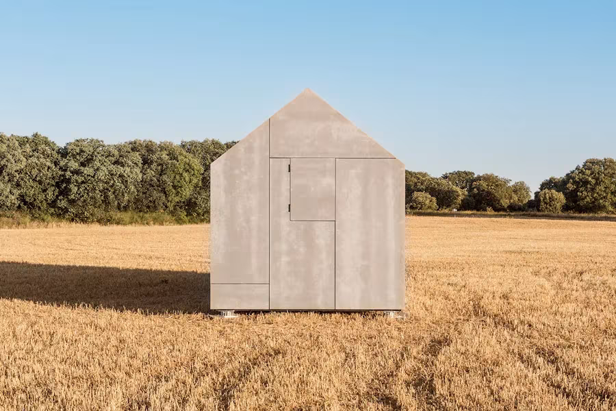 Testero de la casa ÁPH80 de ÁBATON con su silueta de cubierta a dos aguas en un campo de trigo segado