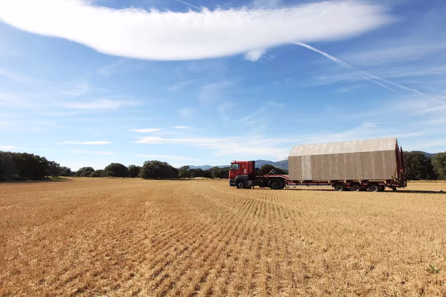 Camión transportando la casa ÁPH80 de ÁBATON por un campo de cereal bajo un cielo azul con nubes