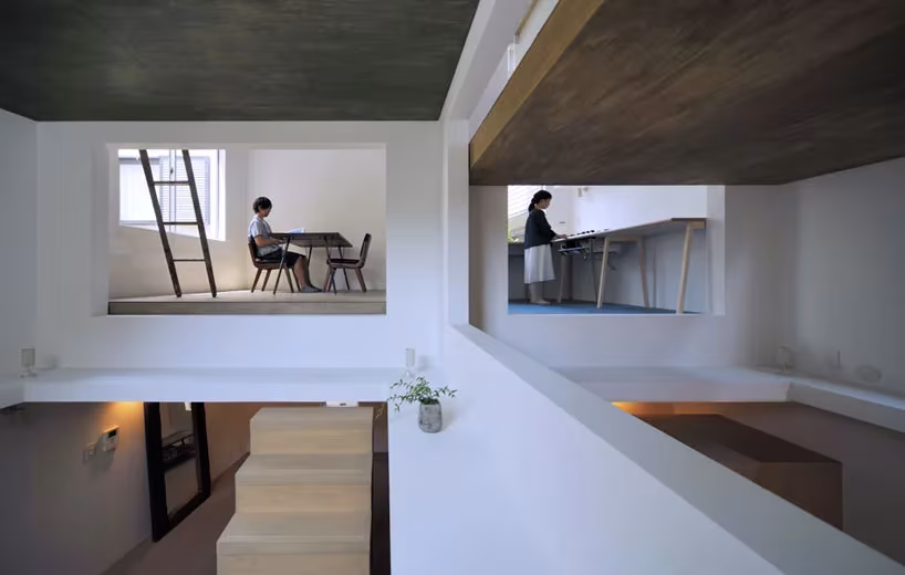 Interior de la House T con huecos que dejan ver dos niveles: una persona en una mesa y una escalera de mano