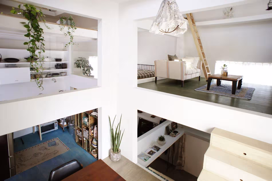 Interior de la House T en varios niveles: salón con sofá blanco, plantas colgantes, escalera de mano y librería abajo