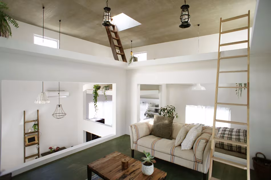 Salón de la House T con sofá de cuadros, techo oscuro con trampilla y dos escaleras de mano de madera