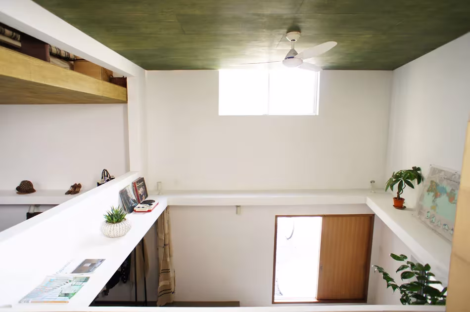 Nivel superior de la House T con estantes blancos, plantas, ventana alta y techo verde oscuro
