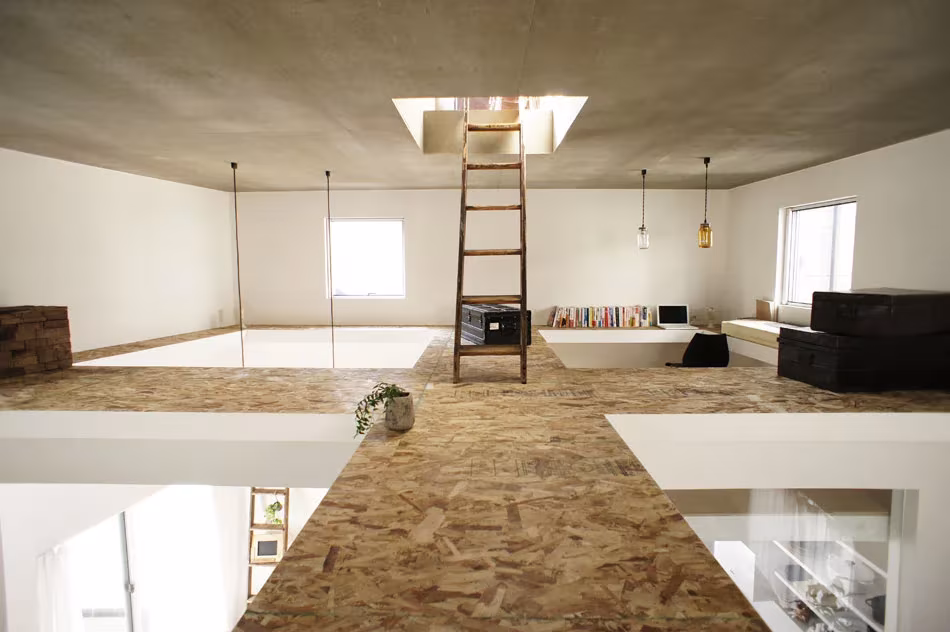 Altillo de la House T con suelo de tablero aglomerado, escalera hacia una claraboya y estantería de libros