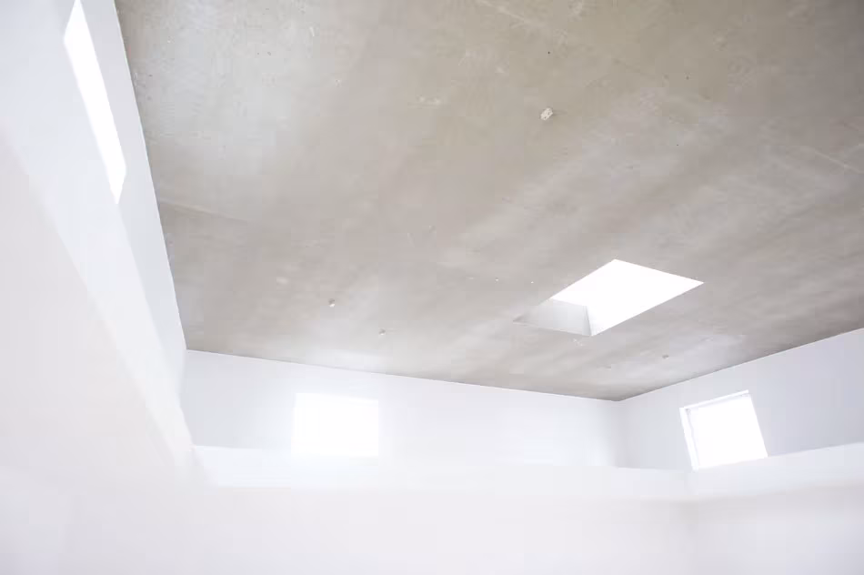 Techo de hormigón claro de la House T con lucernarios y paredes blancas bañadas de luz