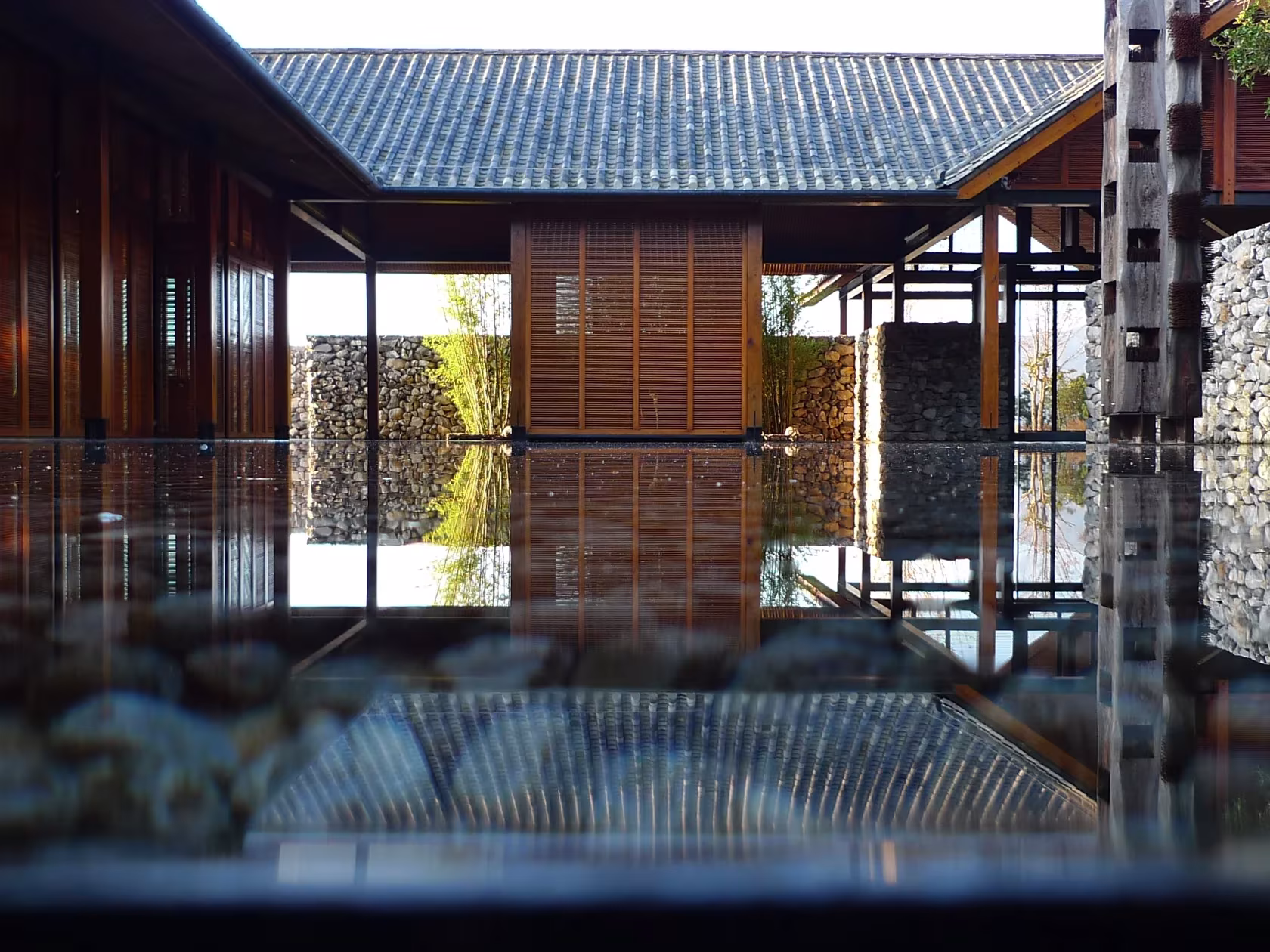 Patio de agua rodeado de pabellones de madera y cubierta de teja, reflejados en The Water House de Li Xiaodong