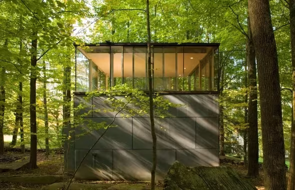 Biblioteca en el bosque de GLUCK+, volumen de paneles grises con remate acristalado entre árboles verdes