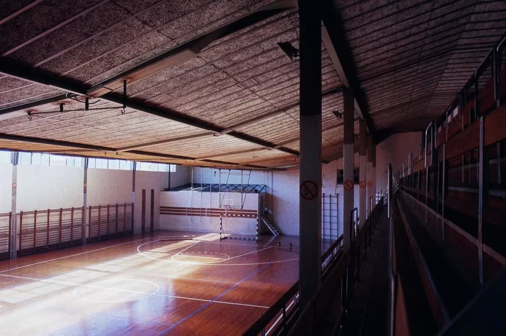 Graderío del Gimnasio Maravillas bajo las cerchas, con vistas a la pista de madera iluminada