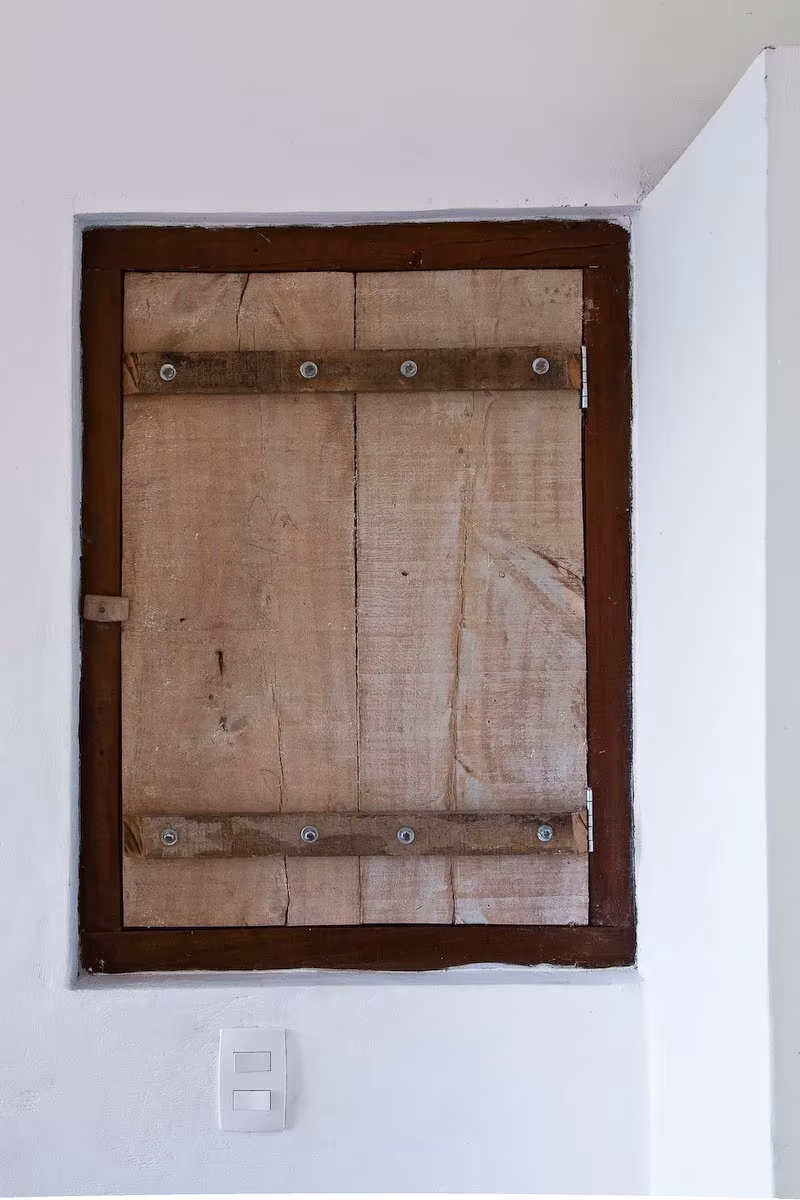 Contraventana de tablas de madera envejecida cerrada en una pared blanca de la Box House