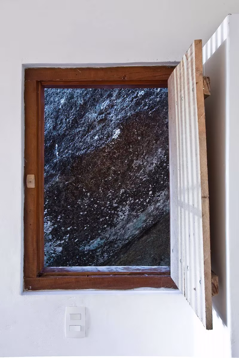 Ventana con marco de madera abierta hacia la roca de granito pegada a la Box House