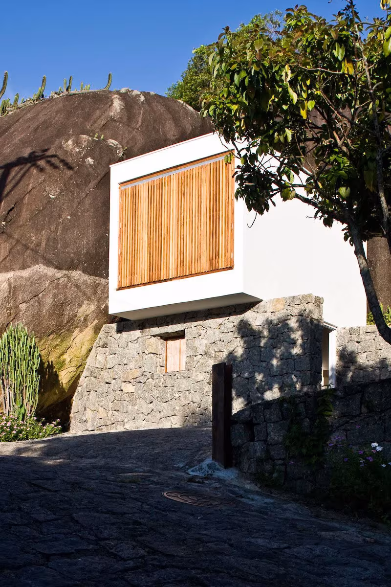 Box House en una isla brasileña: caja blanca con celosía de madera sobre una base de piedra junto a la roca