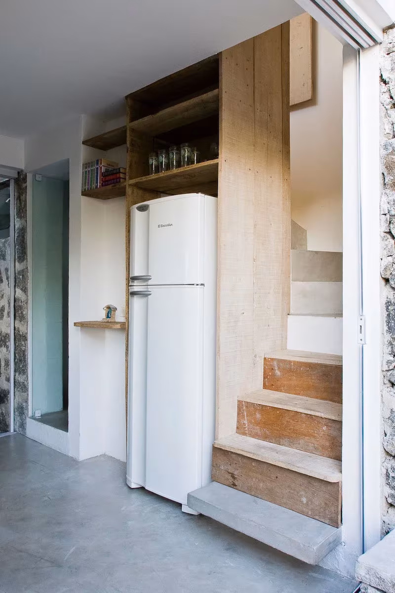 Escalera de madera junto al frigorífico y estantes abiertos que sube a la caja del dormitorio en la Box House